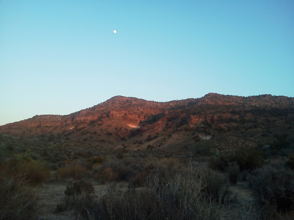 A close-to-full moon sits above the Woods Mountains just before sunset on this hot day