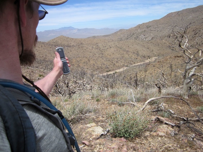 I relax at the top of Hill 1751-T above Butcher Knife Canyon and try my cell phone before hiking down to the sandy wash below