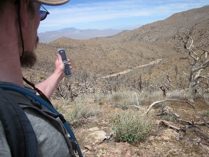 I relax at the top of Hill 1751-T above Butcher Knife Canyon and try my cell phone before hiking down to the sandy wash below
