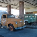 The two antique vehicles are protected from sun and rain under the old gas-station canopy