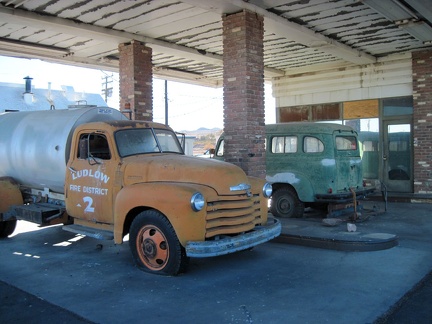 The two antique vehicles are protected from sun and rain under the old gas-station canopy