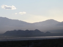 Vehicles on the I-15 freeway, on the other side of Ivanpah Valley, glisten as the setting sun peers through the clouds